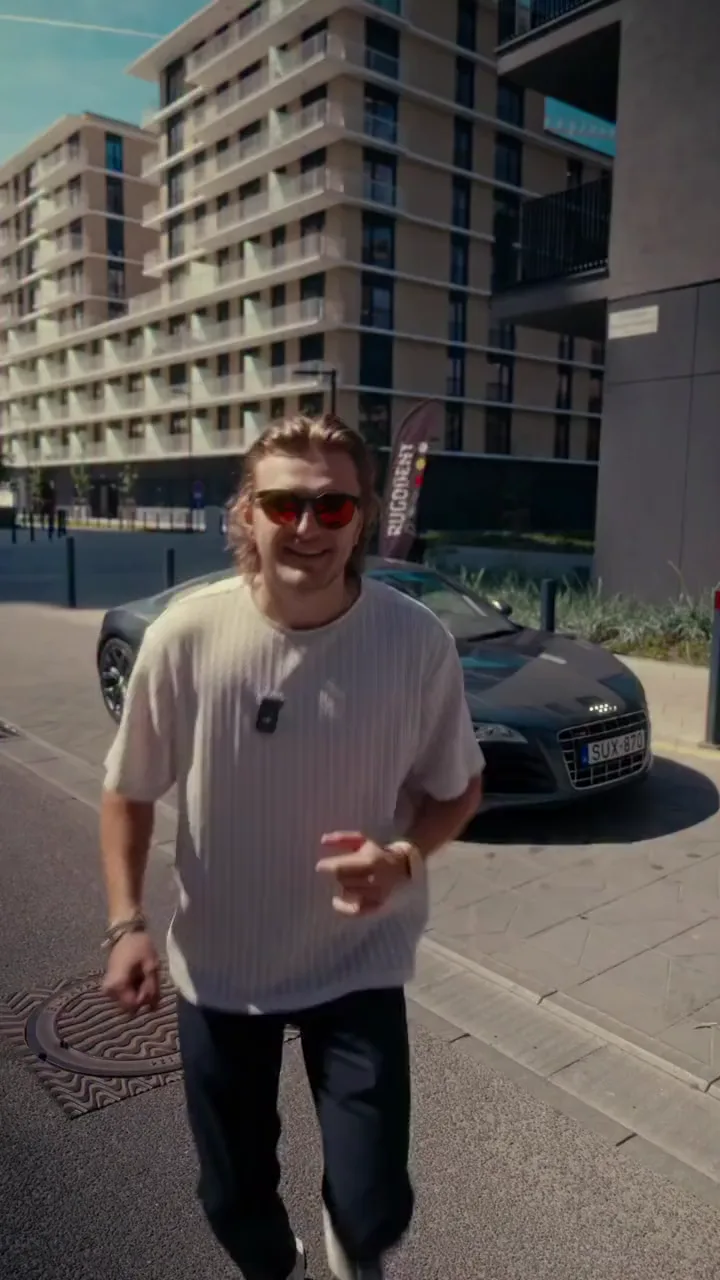 Marci napszemüvegben sétál, mögötte toronyházak, felirat: Nézzétek, Audi R8